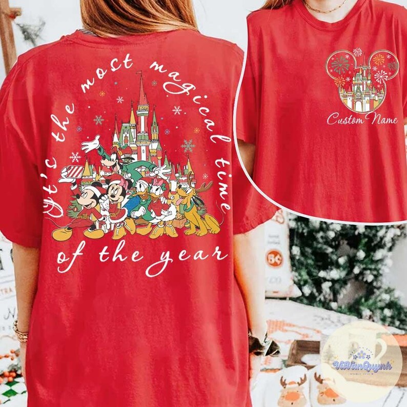 Puede incluir: Camiseta roja con un dise&ntilde;o festivo de Disney. La parte posterior muestra una ilustraci&oacute;n del castillo con Mickey, Minnie, Donald, Daisy y Pluto, con el texto "It's the most magical time of the year." La parte delantera tiene un dise&ntilde;o de castillo y fuegos artificiales.