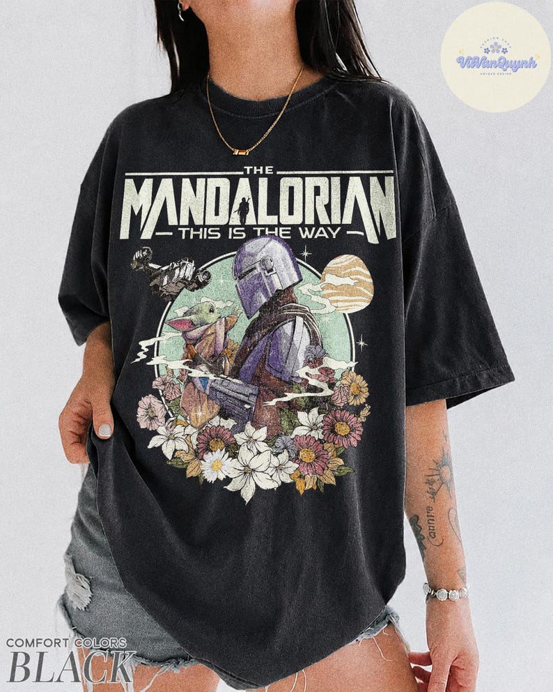 K&ouml;nnte beinhalten: Schwarzes T-Shirt mit einem Aufdruck von The Mandalorian und Grogu, umgeben von Blumen. Der Text "THE MANDALORIAN - THIS IS THE WAY" ist oben aufgedruckt. Das T-Shirt ist schwarz.