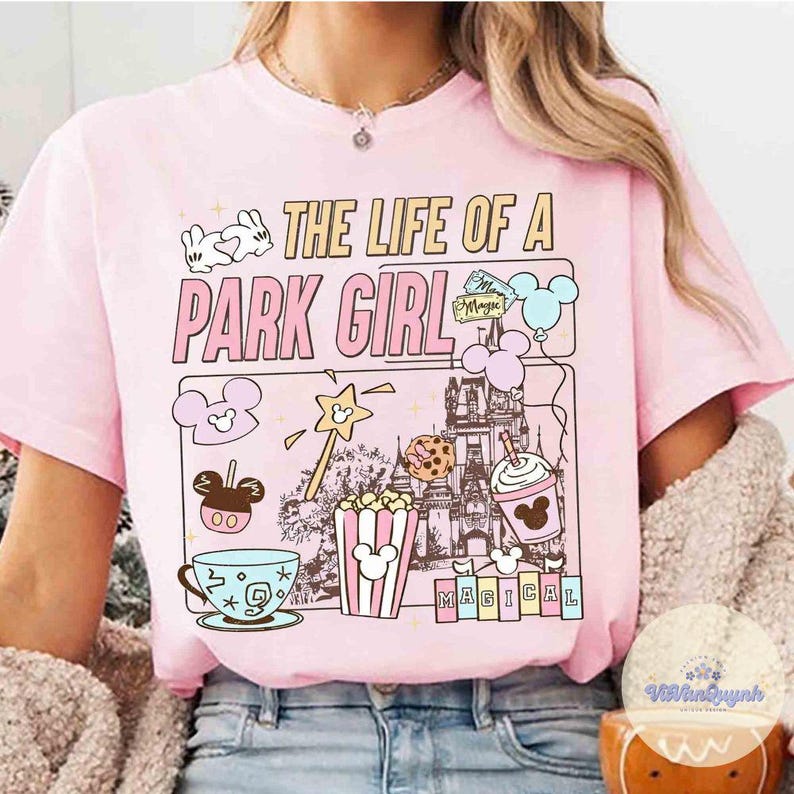 May include: Pink t-shirt with the text "THE LIFE OF A PARK GIRL" and various Disney-themed graphics. The design includes a castle, popcorn, a teacup, and a Mickey Mouse-shaped ice cream bar.