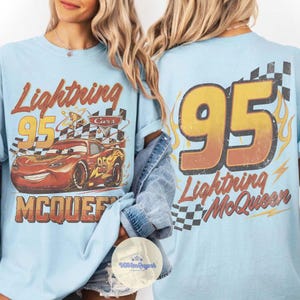 K&ouml;nnte beinhalten: Hellblaue T-Shirts mit Lightning McQueen aus dem Film Cars. Das Design auf der Vorderseite zeigt den Text "Lightning 95 McQueen" mit einer Grafik des Rennwagens. Auf der R&uuml;ckseite steht gro&szlig; "95" und "Lightning McQueen".