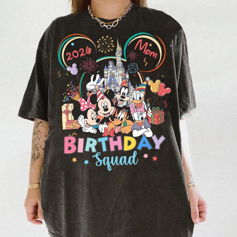 May include: Dark gray t-shirt featuring a colorful graphic of Disney characters, including Mickey and Minnie Mouse, Donald Duck, and Goofy. The shirt has the words "BIRTHDAY Squad" and "Mom" printed on it, with the year "2026".