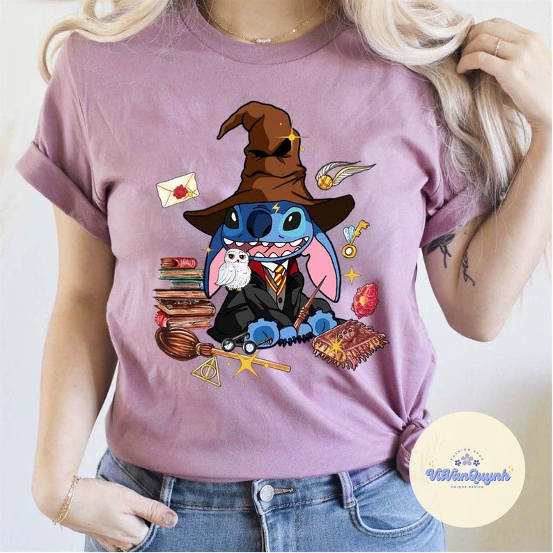 May include: A pink t-shirt featuring a blue Stitch character dressed as a wizard, complete with a brown pointed hat and wand. The design also includes a white owl, books, and other wizarding paraphernalia.
