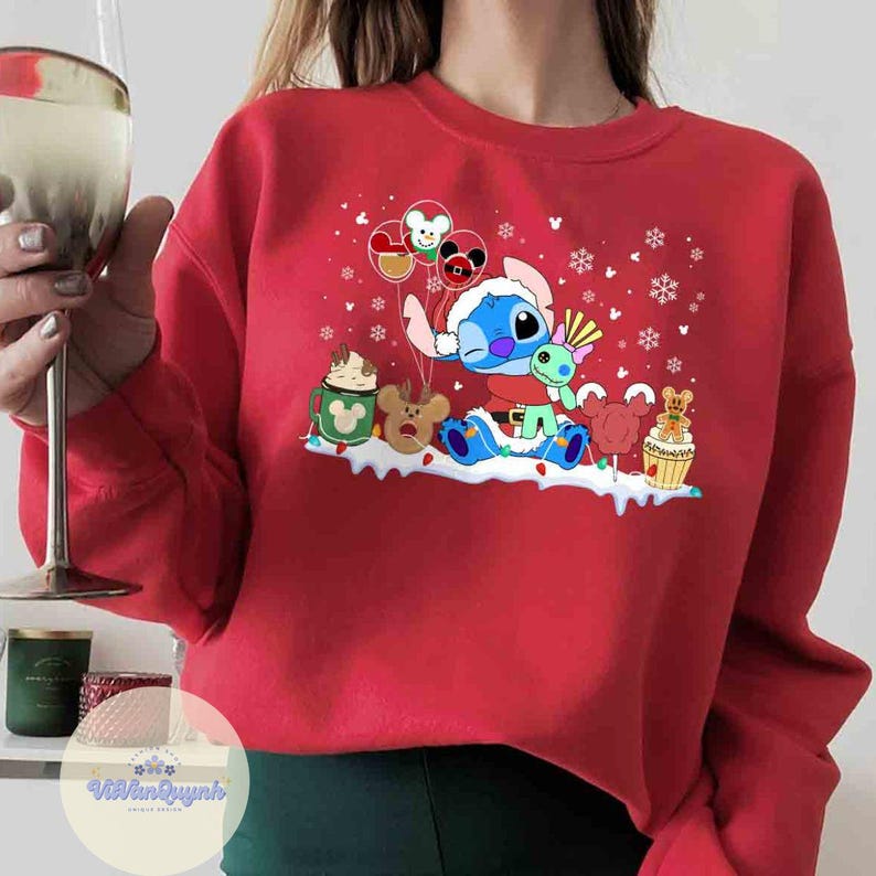 May include: A red sweatshirt featuring a cartoon character with a Santa hat, surrounded by festive elements like snowflakes and character-themed treats. The design includes balloons and other holiday-themed graphics.