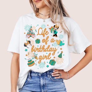 Pu&ograve; includere: T-shirt bianca con una grafica colorata che recita "Life of a birthday girl". Il design include un castello, Minnie Mouse, regali, fuochi d'artificio e una torta di compleanno. Un capo casual per tutti i giorni.