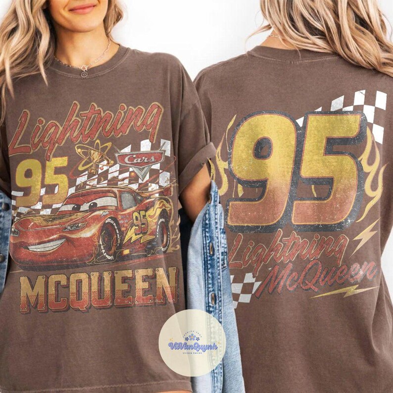 K&ouml;nnte beinhalten: Braunes T-Shirt mit einem Used-Look-Grafik von Lightning McQueen aus dem Film Cars. Das Design umfasst die Nummer 95, den Namen "Lightning McQueen" und eine Zielflagge. Auf der R&uuml;ckseite des Shirts ist ebenfalls die Nummer 95 und der Name zu sehen.