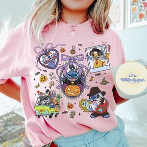 K&ouml;nnte beinhalten: Hellrosa Rundhals-T-Shirt mit einem Halloween-Motiv. Das Design zeigt Cartoon-Figuren in Halloween-Kost&uuml;men, K&uuml;rbisse, Flederm&auml;use und andere gruselige Elemente. Das Shirt hat einen runden Ausschnitt und kurze &Auml;rmel.