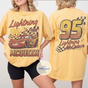 K&ouml;nnte beinhalten: Senfgelbes Lightning McQueen T-Shirt mit der Nummer 95 und dem Charakterbild. Auf der Vorderseite steht "Lightning McQueen" und "Cars". Auf der R&uuml;ckseite steht die Nummer 95 und "Lightning McQueen" mit einem karierten Flaggenmuster.