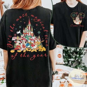 Puede incluir: Camiseta negra con un dise&ntilde;o festivo de Disney, que incluye personajes, un castillo y el texto "It's the most magical time of the year." Tambi&eacute;n se ve un dise&ntilde;o m&aacute;s peque&ntilde;o con un castillo y fuegos artificiales.