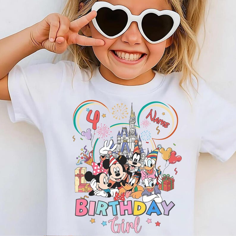 May include: White t-shirt featuring a colorful graphic of Disney characters, a castle, and the text "4" and "Birthday Girl". The design includes Mickey and Minnie Mouse, Donald Duck, and Goofy. The shirt is for a child.
