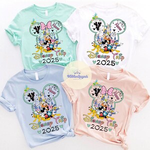 May include: Four short-sleeved t-shirts in pastel colors: mint green, white, light blue, and pink. Each shirt features a Mickey Mouse head design with Disney characters, a bow, and the text "Disney Trip 2025".