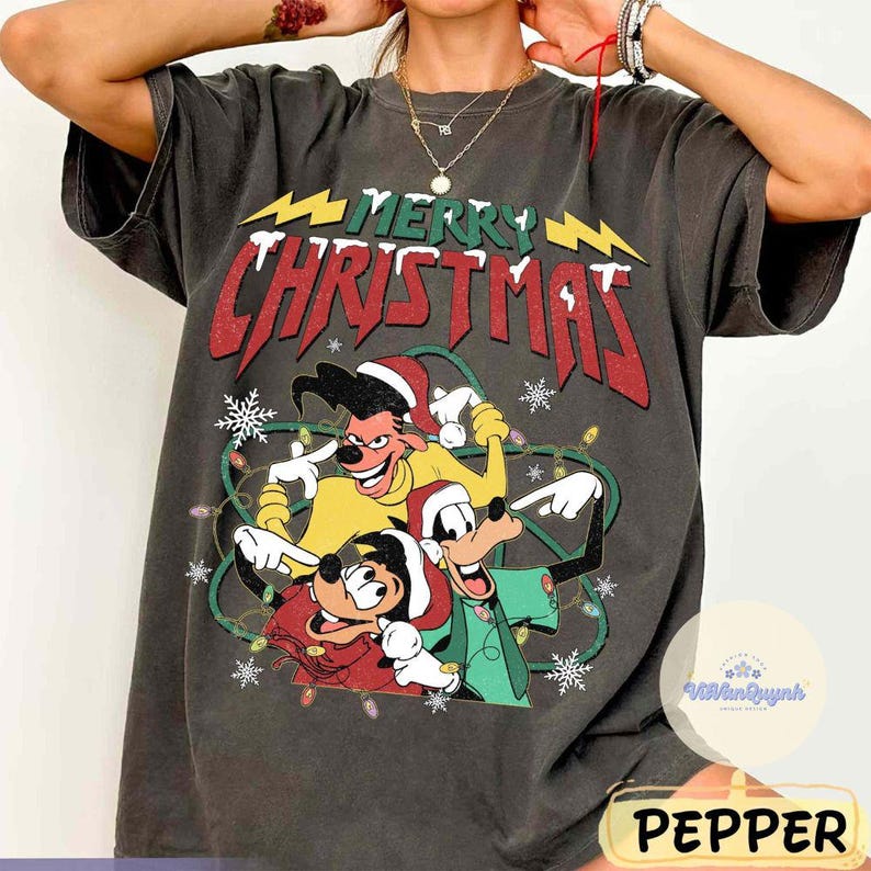 May include: Dark gray t-shirt featuring a festive "Merry Christmas" design with cartoon characters. The graphic includes Goofy, Max, and Pluto in Santa hats, surrounded by Christmas lights and snowflakes. The shirt has a vintage, worn look.