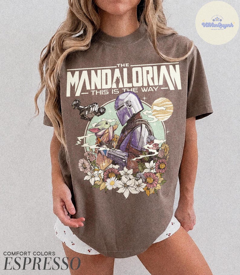 K&ouml;nnte beinhalten: Espressofarbenes T-Shirt mit einer Grafik von The Mandalorian und Grogu, umgeben von Blumen, mit dem Text "THE MANDALORIAN THIS IS THE WAY." Das Shirt ist von der Marke Comfort Colors.