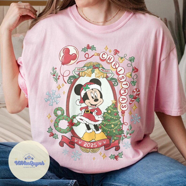 May include: Pink t-shirt featuring a festive Minnie Mouse design. The graphic includes Minnie in a Santa outfit, a Christmas tree, and the words "Christmas" and "Very Merry" in a decorative frame. The year "2025" is also displayed.