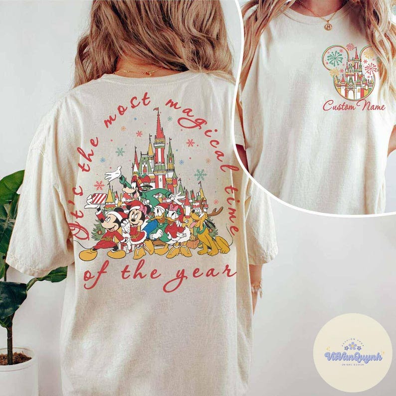 Puede incluir: Camiseta color crema con un dise&ntilde;o festivo de Disney. La parte trasera muestra un castillo y personajes como Mickey y Minnie Mouse, con el texto "It's the most magical time of the year." La parte delantera tiene un dise&ntilde;o m&aacute;s peque&ntilde;o con el texto "Custom Name."