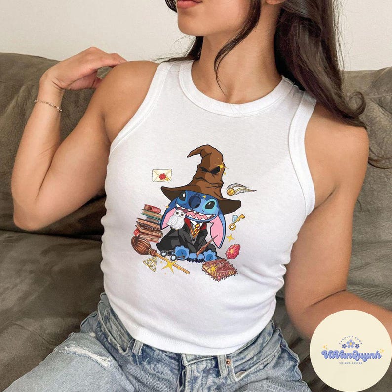 May include: A white tank top featuring a blue Stitch character dressed as a wizard, wearing a brown hat and holding a book. The design includes other wizarding items such as a wand, a book, and a potion bottle. The tank top has a white background and the Stitch character is centrally positioned.