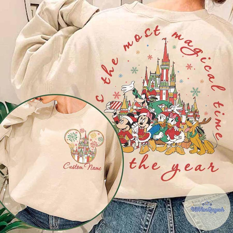 Puede incluir: Sudadera beige con un gr&aacute;fico colorido de personajes de Disney frente a un castillo, con el texto "the most magical time of the year". Una imagen m&aacute;s peque&ntilde;a muestra una cabeza de Mickey Mouse con un castillo y las palabras "Custom Name".