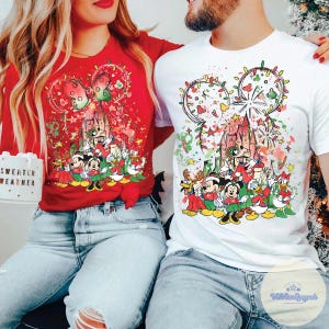 May include: Red and white Christmas-themed t-shirts featuring a Disney character design. The design includes Mickey Mouse, Minnie Mouse, Donald Duck, and other characters in festive attire. The shirts have a castle and fireworks design.