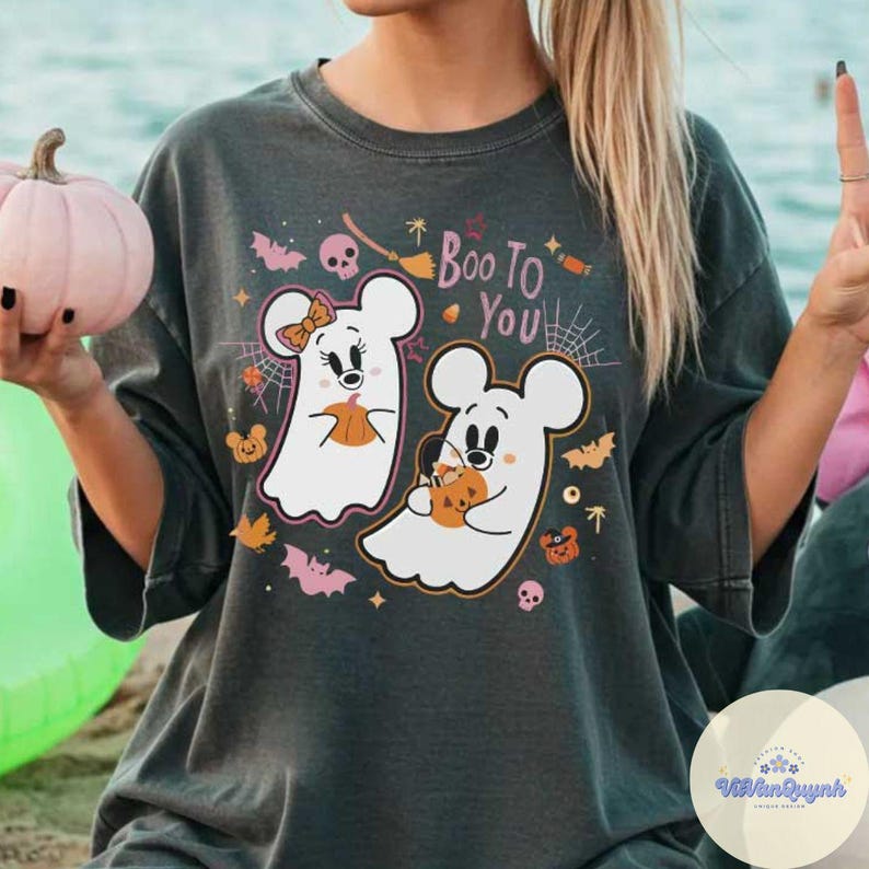 May include: Dark gray t-shirt featuring a Halloween design. The shirt displays two cartoon ghost characters holding pumpkins, with the text "Boo To You" above them. The design includes bats, spiderwebs, and other Halloween-themed graphics.