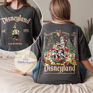 May include: Dark gray t-shirt with "Disneyland" text and a graphic of Mickey Mouse in front of a Christmas tree. The back of the shirt features a Disneyland castle scene with Mickey and friends. "Est. 1955 California" is also printed on the shirt.