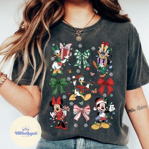 May include: Dark gray t-shirt featuring Disney characters in Christmas attire. Donald Duck, Mickey Mouse, and Minnie Mouse are depicted with gifts, lights, and bows. The shirt has a vintage wash appearance.