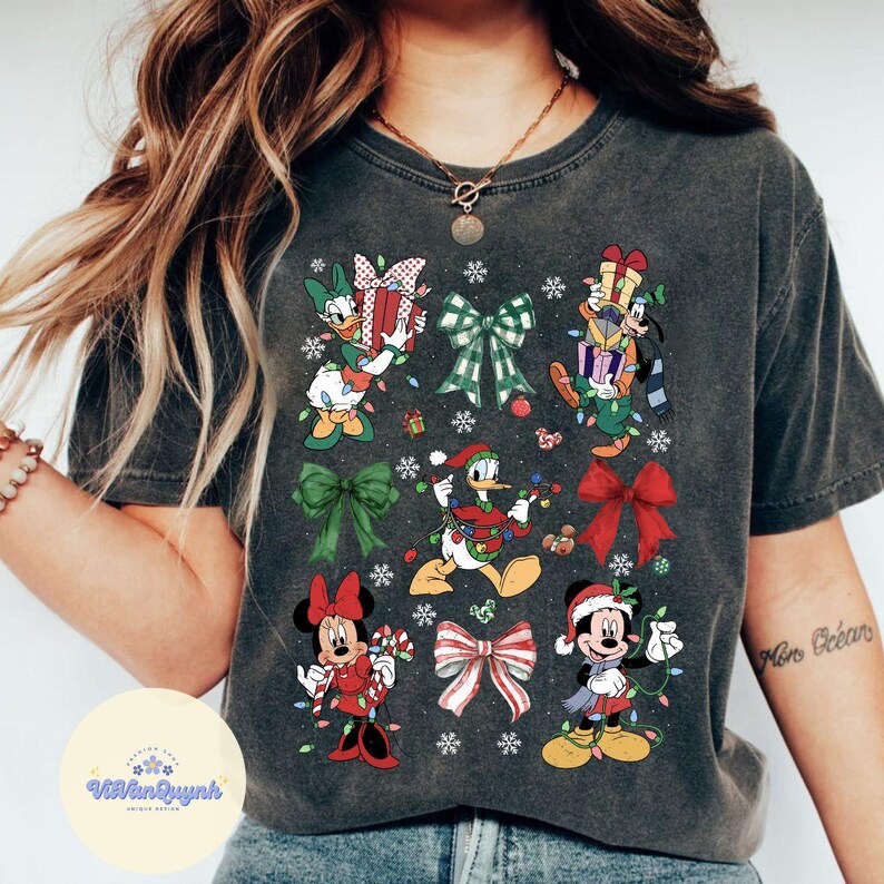 May include: Dark gray t-shirt featuring Disney characters in Christmas attire. Donald Duck, Mickey Mouse, and Minnie Mouse are depicted with gifts, lights, and bows. The shirt has a vintage wash appearance.