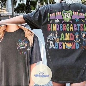 May include: Dark gray t-shirt with a colorful graphic featuring characters and the text "TO KINDERGARTEN AND BEYOND." The design includes Buzz Lightyear, Woody, and other characters. The front of the shirt has a smaller graphic and the letters "UF'26."