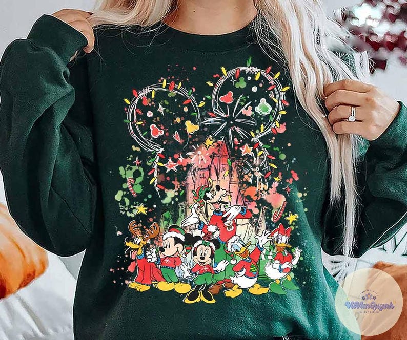 May include: Dark green sweatshirt featuring a festive Disney design. The graphic includes Mickey Mouse ears outlined with Christmas lights, a castle, and several Disney characters in holiday attire. Colorful stars and confetti add to the celebratory theme.