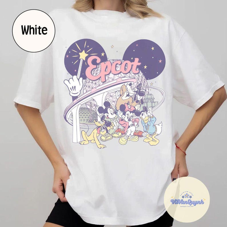 May include: White t-shirt featuring a colorful graphic of Disney characters, including Mickey Mouse, Goofy, and Donald Duck, with the word "Epcot" in pink. The design includes a stylized depiction of a theme park.