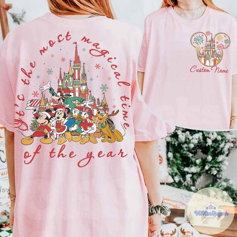 Puede incluir: Camiseta rosa claro con un dise&ntilde;o festivo de Disney. La parte posterior muestra un gr&aacute;fico circular con el texto "It's the most magical time of the year" que rodea un castillo y personajes de Disney. La parte delantera tiene una cabeza de Mickey Mouse con un castillo y las palabras "Custom Name".