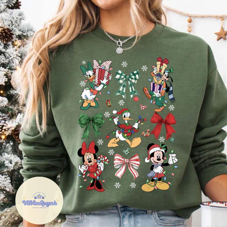 May include: Green sweatshirt featuring Disney characters like Donald Duck, Goofy, and Mickey and Minnie Mouse, each adorned with Christmas lights and bows. The design includes snowflakes and gift boxes, creating a festive holiday theme.