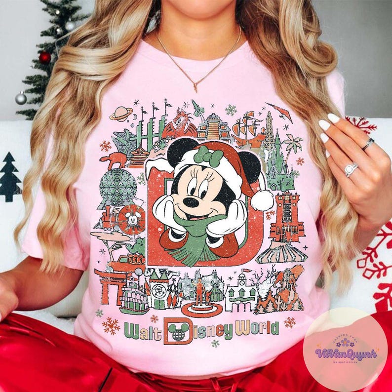 May include: Pink t-shirt featuring a festive Minnie Mouse design with a Santa hat and scarf, surrounded by iconic Walt Disney World landmarks. The text "Walt Disney World" is printed at the bottom in a stylized font.