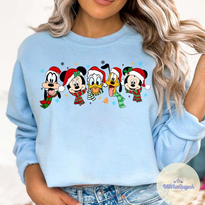 May include: Light blue sweatshirt featuring a festive design with Mickey Mouse, Minnie Mouse, Donald Duck, Goofy, and Pluto. Each character is wearing a Santa hat and a scarf. Snowflakes and a bell are also included in the design.