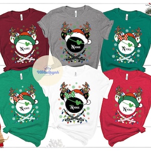 May include: A collection of short-sleeved t-shirts in various colors, including red, gray, green, and white. Each shirt features a festive graphic of a mouse head wearing a Santa hat, reindeer antlers, and a name field. The design includes crossed swords and Christmas lights.