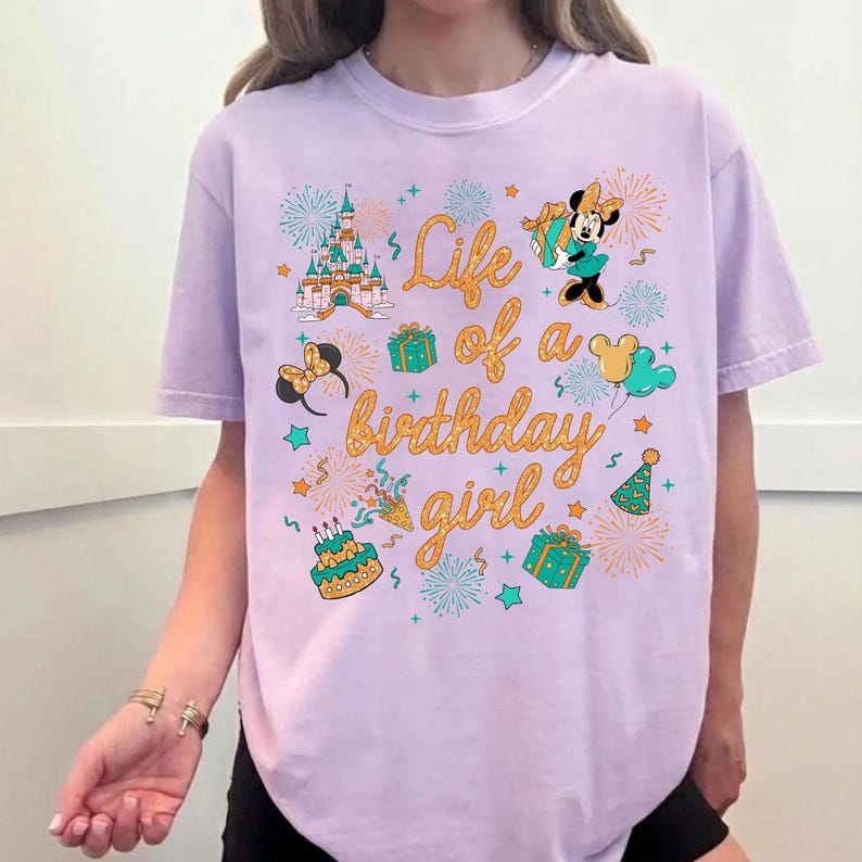 Pu&ograve; includere: T-shirt lilla chiaro con la scritta dorata "Life of a birthday girl". Il design include un castello, Minnie Mouse, regali, palloncini e fuochi d'artificio. Un capo festivo per una festa di compleanno.