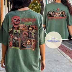 Puede incluir: Camiseta verde con un dise&ntilde;o de Halloween. La parte trasera presenta una calavera, personajes de pel&iacute;culas de terror y el texto "Halloween Horror Nights". La parte delantera tiene personajes de pel&iacute;culas de terror y un globo rojo.