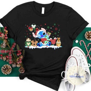 May include: Black t-shirt featuring a cartoon character, Stitch, in a Santa hat, surrounded by Christmas-themed graphics. The design includes balloons, snowflakes, and festive treats. White sneakers are visible in the bottom right corner.