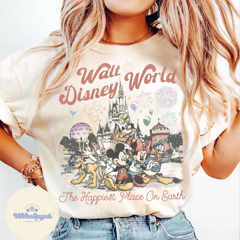 K&ouml;nnte beinhalten: Cremefarbenes Sweatshirt mit einer Disney-Grafik, die Micky Maus, Minnie Maus und Donald Duck vor dem Cinderella-Schloss zeigt. Der Text "Walt World Disney" und "The Happiest Place On Earth" ist auf der Vorderseite aufgedruckt.
