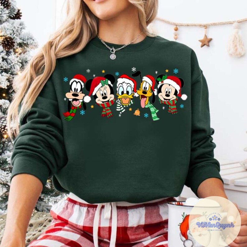 May include: Dark green sweatshirt featuring a festive graphic of Disney characters, including Mickey Mouse, Minnie Mouse, Donald Duck, Goofy, and Pluto, all wearing Santa hats and scarves. The design includes snowflakes and a bell.