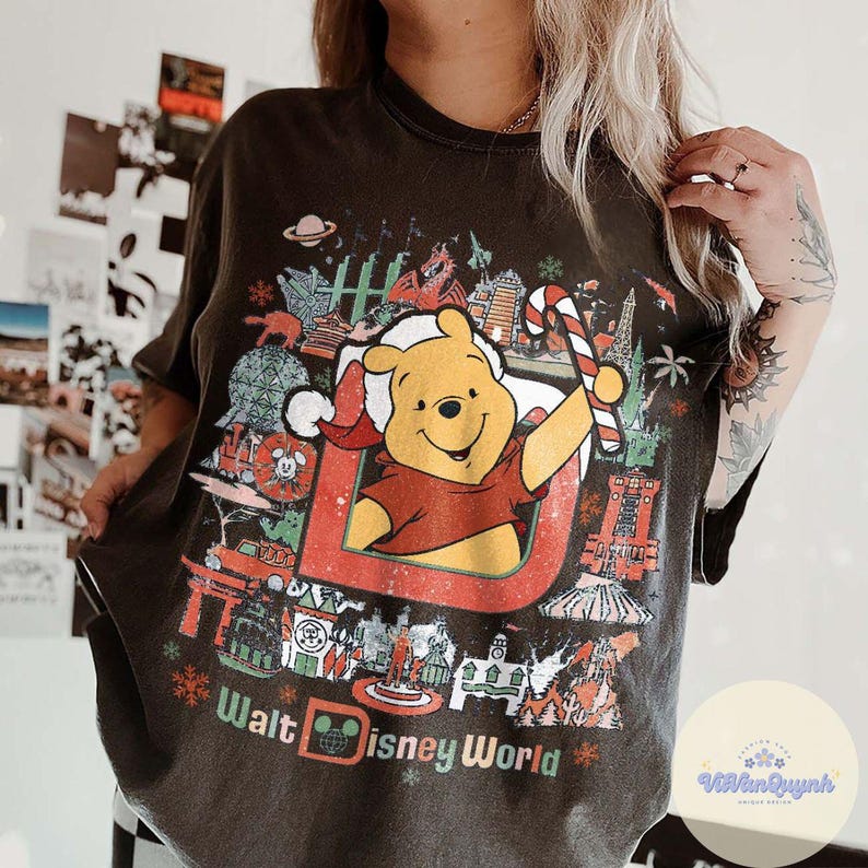 May include: Dark gray t-shirt featuring a graphic of Winnie the Pooh in a Santa hat holding a candy cane, with the text "Walt Disney World." The design includes various Disney World landmarks and snowflakes.