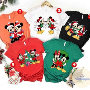 Op de afbeelding: Een verzameling van vijf t-shirts met korte mouwen met Mickey en Minnie Mouse in kerstthema's. De shirts zijn in verschillende kleuren, waaronder oranje, wit, zwart, rood en groen. Elk shirt heeft een andere afbeelding van de iconische personages.
