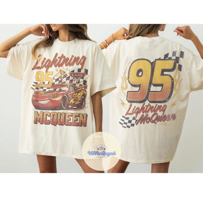 K&ouml;nnte beinhalten: Cremefarbenes T-Shirt mit einem Lightning McQueen-Motiv aus dem Film Cars. Auf der Vorderseite sind die Nummer 95, eine Zielflagge und der Name "McQueen" zu sehen. Auf der R&uuml;ckseite stehen ebenfalls "95" und "Lightning McQueen".