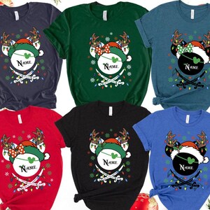 May include: A collection of Christmas-themed t-shirts in various colors, each featuring a festive design. The design includes a mouse head wearing a Santa hat and reindeer antlers, with the word "Name" and crossed swords.