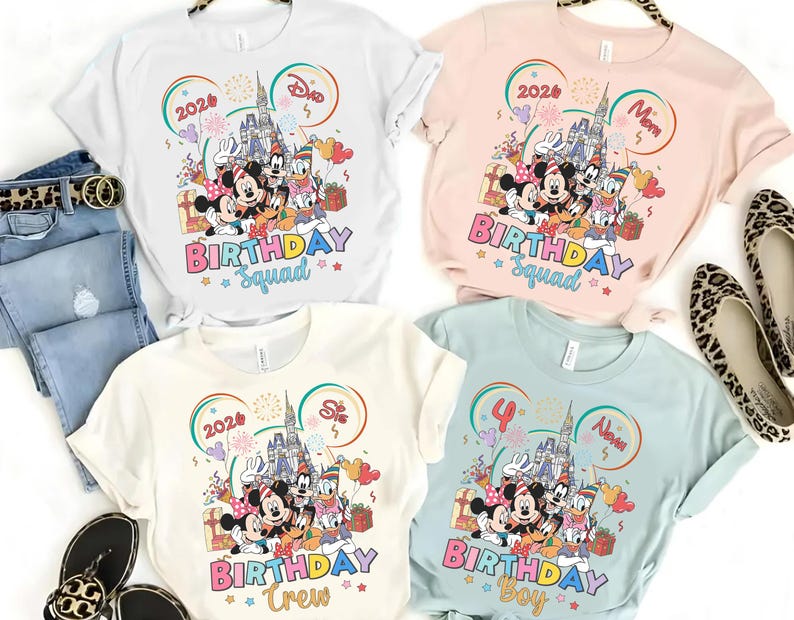May include: Four t-shirts in white, pink, cream, and light blue, each featuring a colorful graphic of Disney characters in front of a castle. The shirts have the words "BIRTHDAY Squad", "BIRTHDAY Crew", and "BIRTHDAY Boy" printed on them.