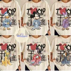 K&ouml;nnte beinhalten: Cremefarbene T-Shirts mit Disney-Figuren in traditioneller japanischer Kleidung. Jedes Shirt zeigt "Disneyland TOKYO" mit einer Grafik einer Pagode und eines Torii-Tors. Zu den Figuren geh&ouml;ren Donald Duck, Mickey Mouse, Daisy Duck, Pluto und Goofy.