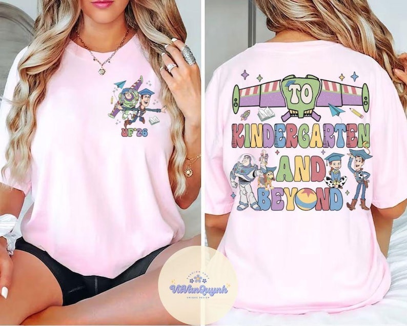 May include: Light pink t-shirt featuring a colorful graphic of characters and text from the movie Toy Story. The front of the shirt has a small graphic with the text "UF '26". The back of the shirt has the text "TO KINDERGARTEN AND BEYOND".