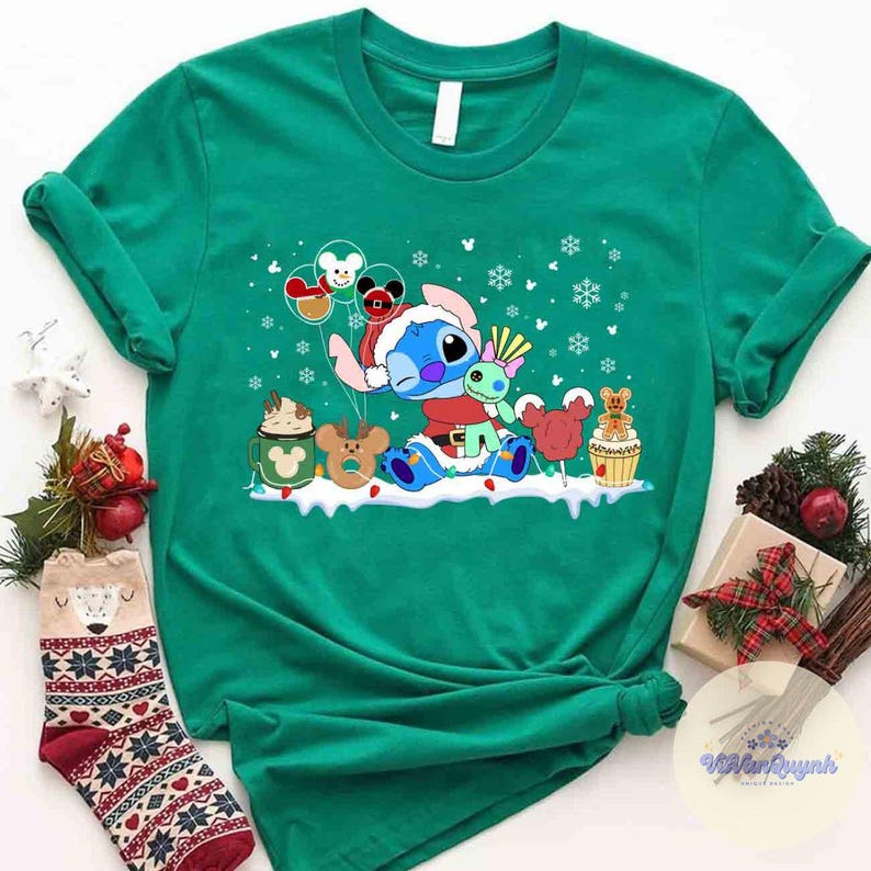 May include: A green t-shirt featuring a cartoon Stitch character in a Santa hat and suit, surrounded by Christmas-themed graphics. The design includes snowflakes, balloons, and festive treats. The shirt is paired with Christmas socks.