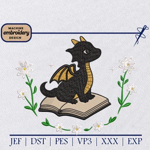 Op de afbeelding: Zwart drakenborduurontwerp met gouden details, zittend op een boek. Het ontwerp bevat de tekst "MACHINE EMBROIDERY DESIGN" en is omgeven door witte bloemen en groene stelen.