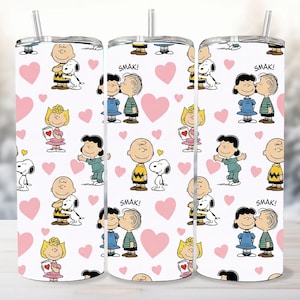 Puede incluir: Tres vasos blancos de acero inoxidable con un patrón repetido de personajes de Peanuts, corazones rosas y la palabra "Smak!". Los vasos tienen una tapa plateada y una pajita.