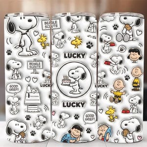 Könnte beinhalten: Ein weißer Becher mit Snoopy und anderen Peanuts-Charakteren. Das Design umfasst Snoopy mit Kuchen, Pfotenabdrücke und die Wörter "Lucky", "Good Grief" und "Beagle Scouts."
