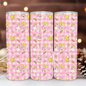 Könnte beinhalten: Drei Edelstahlbecher mit einem rosa Vichy-Muster mit Cartoon-Enten, Pilzen und Blumen. Das Design wiederholt sich über die Oberfläche der Becher. Die Becher sind zylindrisch und scheinen isoliert zu sein.